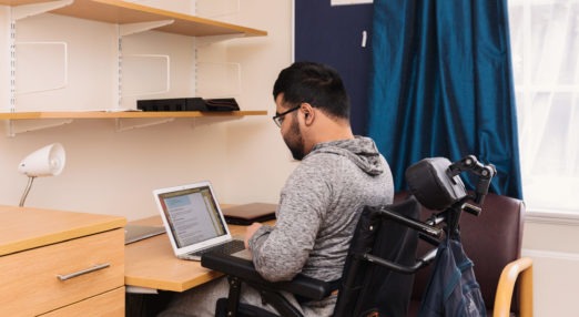 Goodenough College Member in a wheelchair by his desk with a laptop