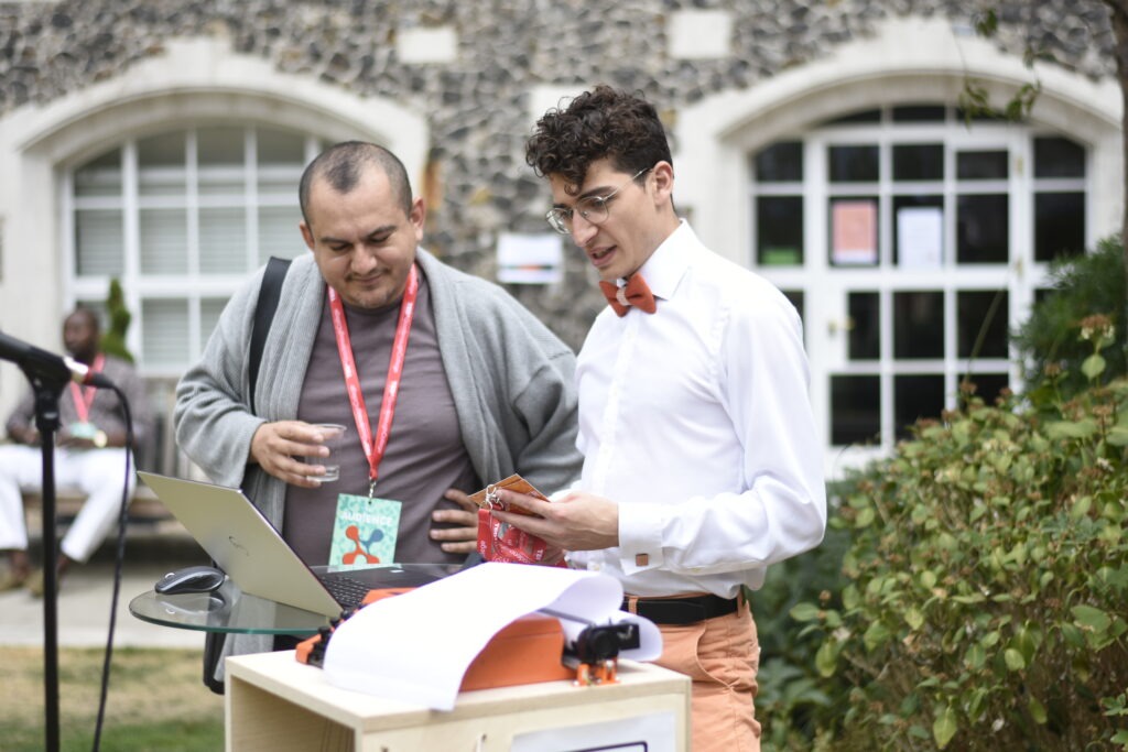 Two men look at an AI typewriter at the TEDxGoodenoughCollege event